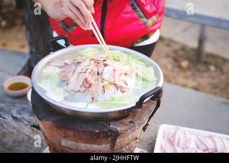 Mettere a fuoco sul ventre di maiale, la donna sta usando i bastoncini di chopsticks per tenere il maiale sulla padella Foto Stock