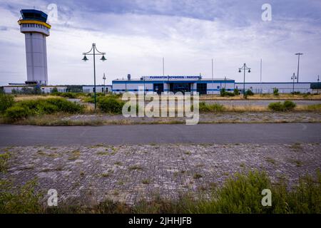 Parchim, Germania. 18th luglio 2022. L'edificio del terminal si trova dietro un parcheggio parzialmente sovrastato all'ex aeroporto. Dopo essere stato acquistato da un investitore cinese, l'ex aeroporto militare dell'esercito russo doveva essere sviluppato in un centro di volo internazionale del carico. Dopo l'insolvenza dell'operatore nel maggio 2019, le operazioni di volo sono cessate e gli impianti all'aperto sono parzialmente sopravallevati. Credit: Jens Büttner/dpa/Alamy Live News Foto Stock