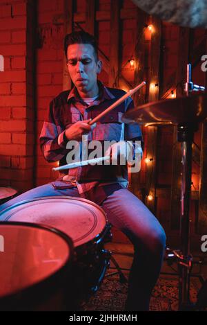 Giocatore maschio serio con bastone di legno che suona la batteria sul palco durante la performance dal vivo nel club scuro Foto Stock