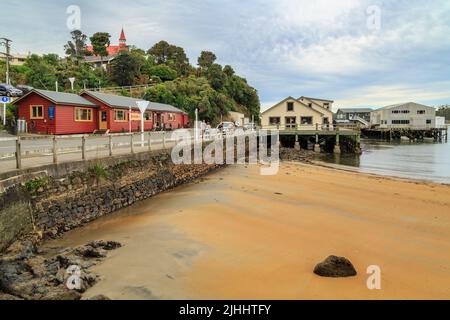 Il lungomare del piccolo insediamento di Oban o Halfmoon Bay a Stewart Island, Nuova Zelanda. Sulla collina si trova la storica chiesa presbiteriana Foto Stock