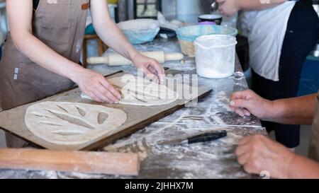 Un panettiere forma e taglia il tradizionale pane francese di Fougasse. Vista frontale. Foto Stock