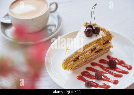 Torta al biscotto di ciliegia, lampone, tazza di cappuccino su tavola di legno all'esterno. Decorazioni di fiori rosa nella terrazza della caffetteria. Niente zucchero, dolci naturali. Foto Stock