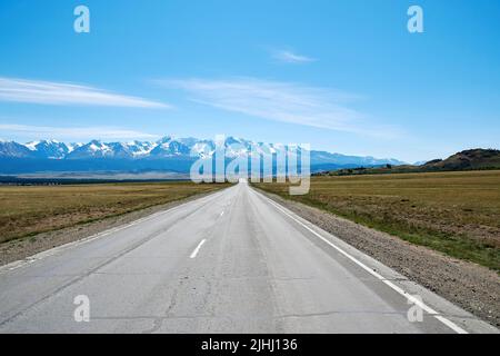 Una strada diritta va in lontananza in una catena montuosa innevata. Paesaggio panoramico sfondo. Montagne di Altai Foto Stock