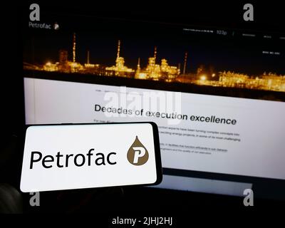 Persona che tiene il cellulare con il logo della società britannica di servizi energetici Petrofac Limited sullo schermo di fronte alla pagina web. Mettere a fuoco sul display del telefono. Foto Stock