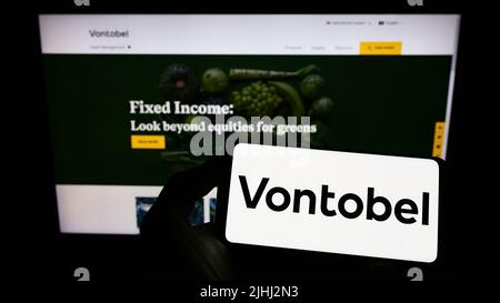 Persona che tiene sullo schermo uno smartphone con il logo della società finanziaria svizzera Vontobel Holding AG davanti al sito. Mettere a fuoco sul display del telefono. Foto Stock