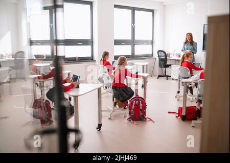 Vista posteriore, classe di studenti seduti e che ascoltano l'insegnante in aula Foto Stock