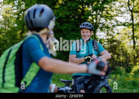Ritratto di coppia attiva in bicicletta al parco estivo, in piedi sul sentiero e guardando la macchina fotografica Foto Stock