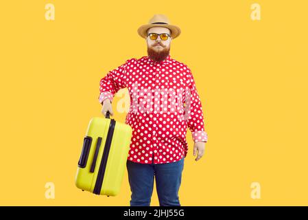 Uomo elegante e chic con espressione seria che tiene la valigia pesante su sfondo arancione. Foto Stock