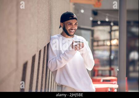 Bell'uomo in un berretto nero con uno smartphone per strada Foto Stock