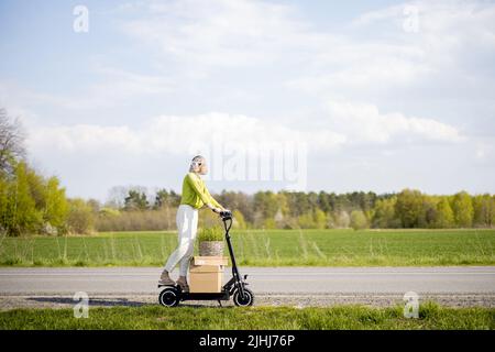 Donna che guida scooter elettrico con parcelle sulla strada da campo Foto Stock