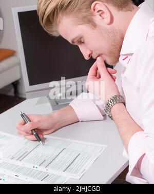 il giovane lavora sodo alla dichiarazione fiscale sulla scrivania Foto Stock