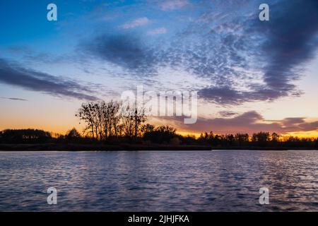 Nuvole colorate dopo il tramonto sul lago e gli alberi sulla riva Foto Stock