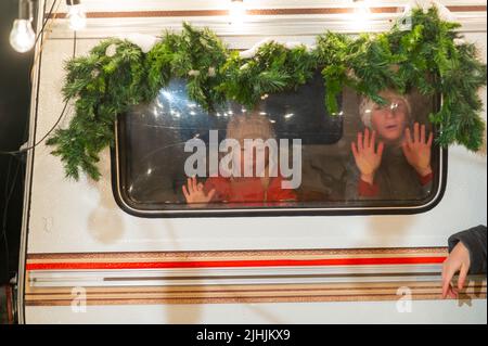 Due ragazzi guardano fuori dalla finestra di un camper decorato a Natale. Foto Stock