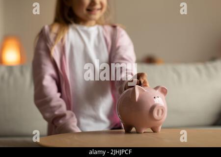 Piccola ragazza irriconoscibile che mette la moneta in Piggybank a casa Foto Stock