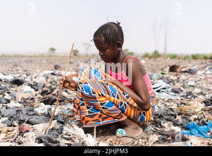 La giovane ragazza africana che vistosamente si infiltra in un mucchio di rifiuti, costretta a cercare materiali salabili; concetto di lavoro minorile Foto Stock