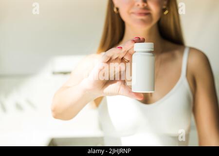 Una giovane donna sta tenendo un vaso bianco di vitamine o pillole. Luogo per il vostro logo Foto Stock