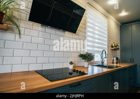 Piano di lavoro in cucina moderna con stufa elettrica, cappa aspirante, lavello e armadi a incasso con elettrodomestici e utensili da cucina. Foto Stock