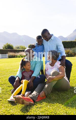 Famiglia multirazziale che parla mentre si gode il tempo libero sul campo contro il cielo limpido Foto Stock