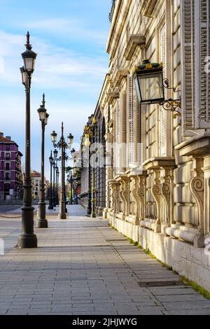 Marciapiede della strada del Palazzo reale di Madrid con lampioni di strada e vecchio edificio in giornata di sole. Spagna. Foto Stock