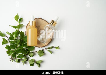 Due bottiglie di siero facciale o olio essenziale che giacciono su un piatto di legno in un salone di cosmetologia Foto Stock