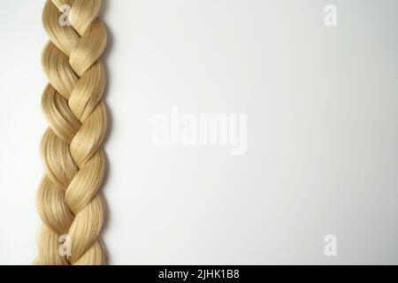 Un filo di capelli biondi adagiato su sfondo bianco Foto Stock