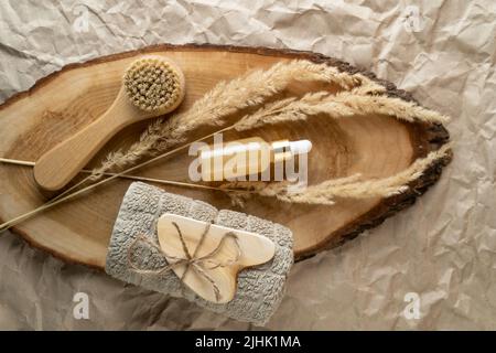 Una bottiglia contagocce di siero o olio con vitamina C e una spazzola per il viso e un massaggiatore di guasha adagiato su un vassoio di legno Foto Stock
