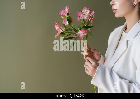 vista croppata della donna in bianco blazer che tiene fiori di alstroemeria isolato sul verde Foto Stock