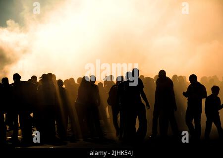 Silhouette di gruppo di persone circondato da fumo pesante da pneumatici bruciati. Evento auto, gara di deriva, pubblico in concetti di fumo. Foto Stock