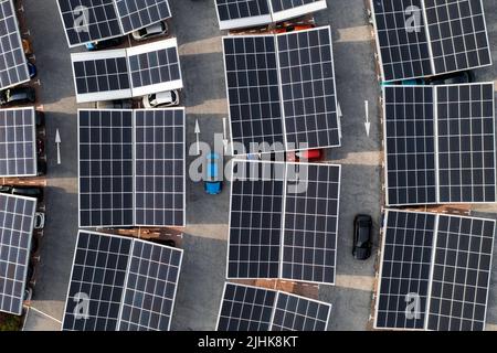 Vista aerea direttamente sopra auto elettriche parcheggio sotto pannelli solari su un parcheggio tetto pronto per la ricarica Foto Stock