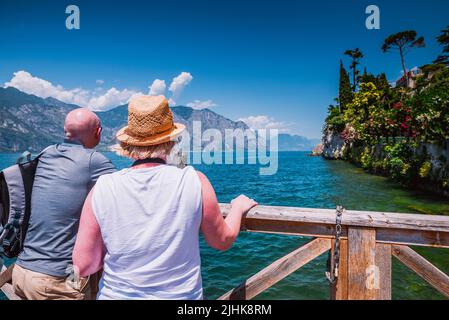 Coppia turistica che guarda al Lago di Garda da un molo di legno. Malcesine è un comune della provincia di VE, situato sulla sponda orientale del Lago di Garda Foto Stock