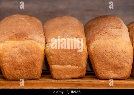 Primo piano di pane appena sfornato su ripiani in legno, vista frontale. Produzione di prodotti da forno Foto Stock
