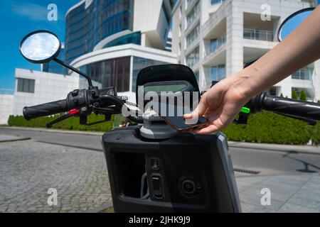 La mano di una donna che utilizza un telefono cellulare scansiona il codice QR su uno scooter motociclistico in una giornata di sole. Concetto di noleggio di trasporto Foto Stock