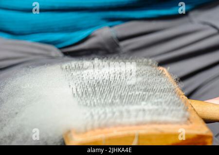 Una donna utilizza pettini tradizionali per cartoncino per preparare la lana di pecora per la filatura. Foto Stock