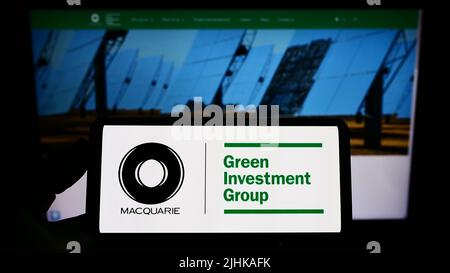 Persona che tiene lo smartphone con il logo della società Green Investment Group Limited (CONCERTO) sullo schermo di fronte al sito Web. Mettere a fuoco sul display del telefono. Foto Stock