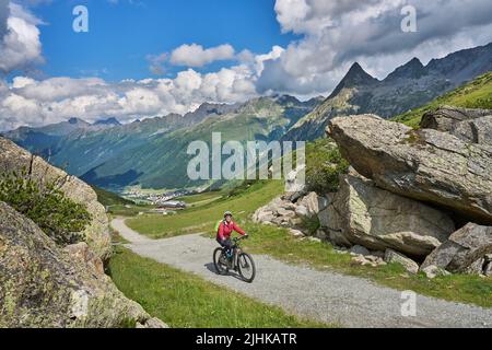 Bella attiva donna anziana che guida la sua mountain bike elettrica nella catena montuosa silvretta sopra il lago barriera Kopssee, vicino a Gaschurn, Tirolo, Austria Foto Stock
