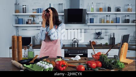 donna che strofinava gli occhi irritati vicino alla cipolla tritata sul tagliere Foto Stock