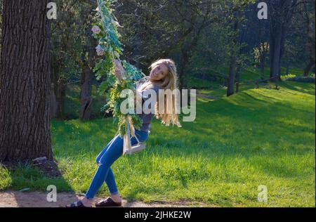 Una giovane donna ama oscillare su un'altalena all'aperto decorata con fiori. Foto Stock