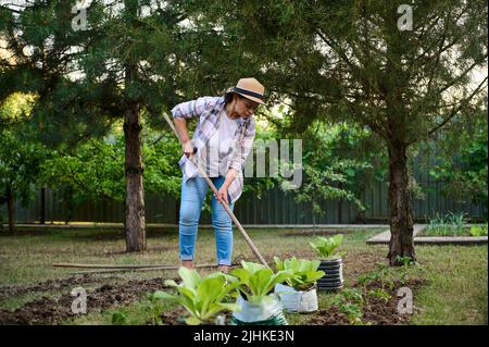 Ritratto di una donna ispirata agricoltore orticulturista scavando terreno mentre il giardinaggio nella fattoria biologica. Concetto di giardinaggio Foto Stock