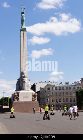 Riga turismo; i turisti in un tour in segway arrivano al Monumento della libertà nel centro della città; riga, Lettonia, Europa; viaggio in Lettonia. Foto Stock