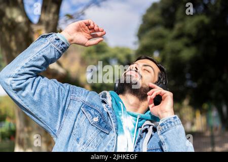 Giovane uomo latino che ascolta musica all'aperto con le cuffie. Espressione di felicità, atteggiamento vincente. Foto Stock