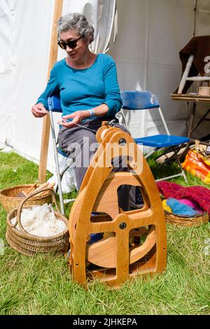Una donna gira la lana usando una versione moderna di una ruota che gira tradizionale. Foto Stock