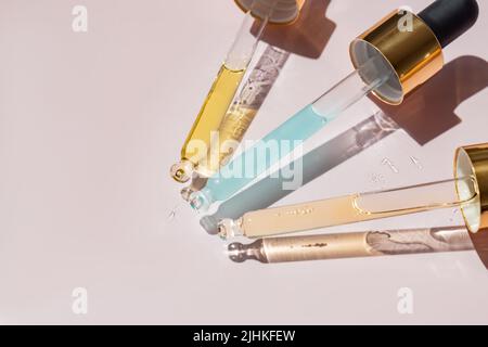 Primo piano delle pipette con versamento di olio essenziale liquido o siero su sfondo rosa. Contagocce con una goccia di caduta di olio di aromaterapia. Foto Stock