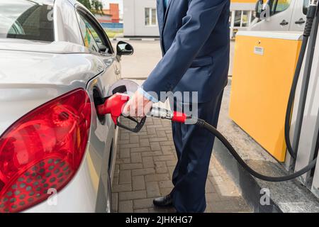 Uomo d'affari senior in piedi sulla stazione di servizio e auto di rifornimento. Foto Stock