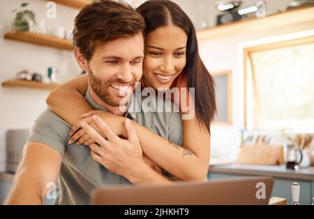 Giovane coppia interrazziale felice legame mentre usando un portatile insieme a casa. Fidanzata caucasica e ragazza che guarda lo schermo del computer Foto Stock