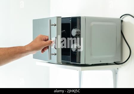 Porta a microonde chiusa a mano e con forno a microonde per cucinare in cucina Foto Stock