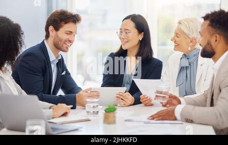 Felici i giovani e diversi colleghi che discutono insieme piani e idee su un tablet digitale durante una riunione in una sala riunioni d'ufficio. Asiatico Foto Stock