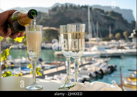 Versando in tre bicchieri di champagne francese spumante e vista sulle colorate barche di pescatori nel vecchio porto di Cassis, Provenza, Francia, estate Foto Stock