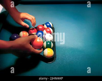 Mani che preparano le palle da biliardo in rastrelliera triangolare sul tavolo da biliardo Foto Stock