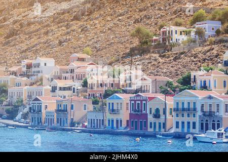 Vista panoramica sulle case tradizionali e colorate e sul porto chiamato Yalos con le barche a vela nell'isola di Symi Dodecanese, in Grecia. Tonalità. Foto Stock