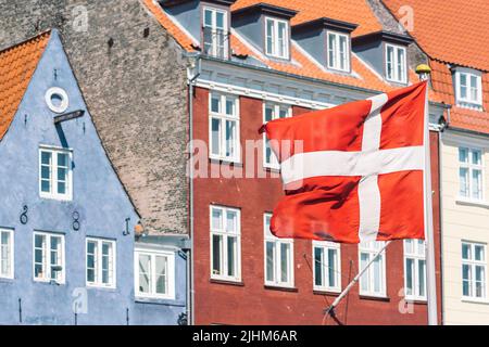 Facciata colorata di vecchie case tradizionali lungo il canale Nyhavn o il nuovo porto, il canale e il quartiere dei divertimenti di Copenhagen con bandiera danese Foto Stock